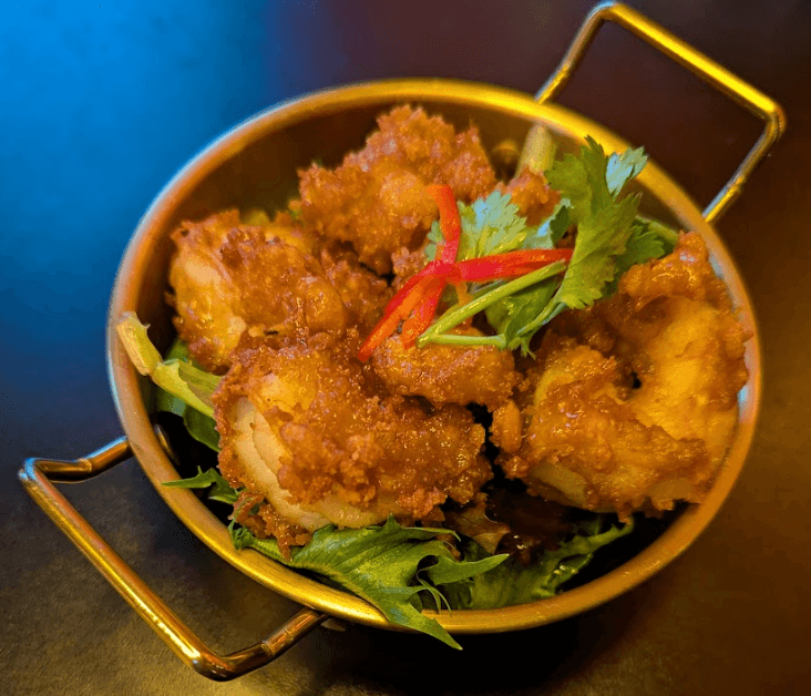 Five pieces of crispy popcorn shrimp at Khao, partially unbreaded, served with sauce on a white plate