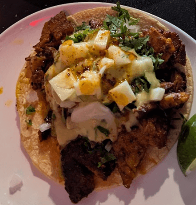 Taco al pastor from Torta Boyz topped with pineapple, onions, cilantro, and creamy sauce on a double corn tortilla