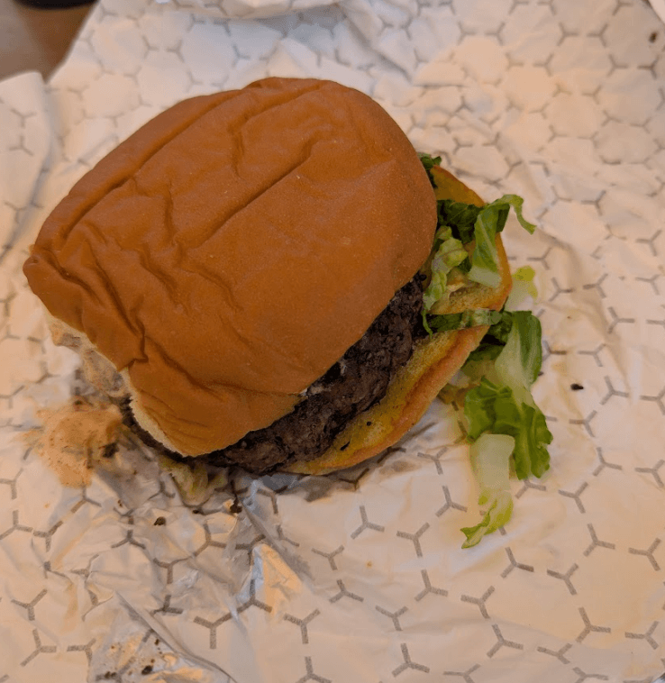 A plain-looking beef burger with lettuce in a soft bun, served on branded wrapping paper from Baja Burger Shack.