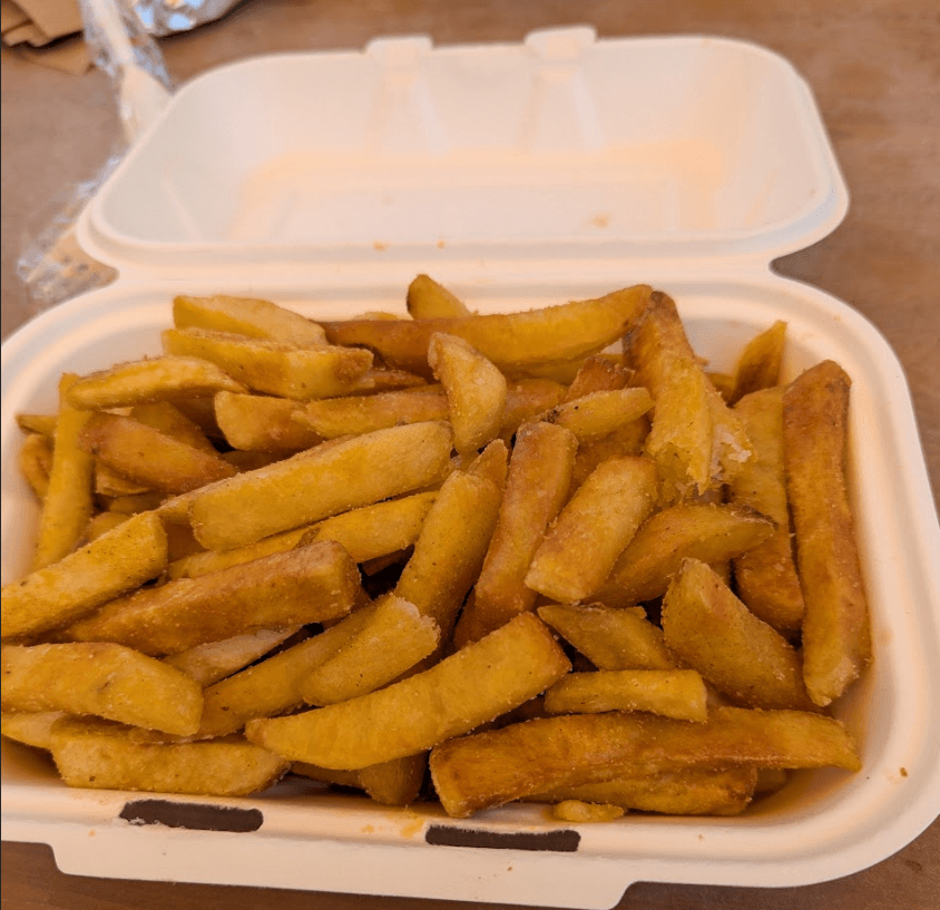 A generous portion of golden, crispy fries in a white takeout container from Baja Burger Shack.