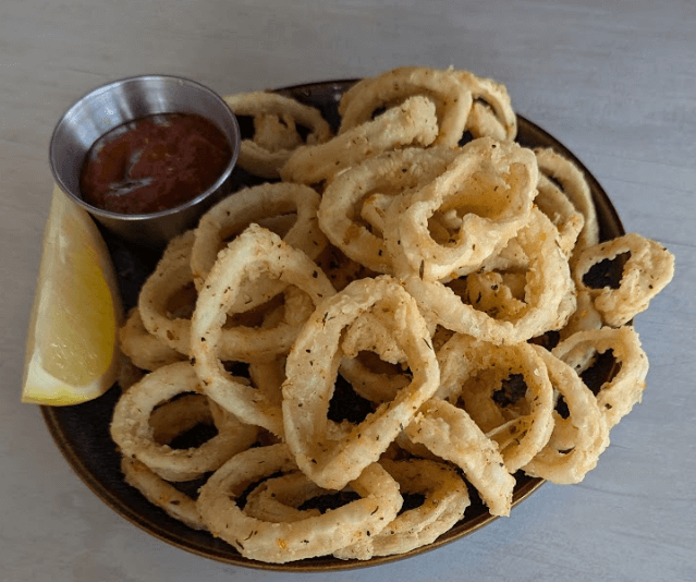 A crispy fried calamari appetizer served with a lemon wedge and marinara dipping sauce on a dark plate at Seafood Grill.